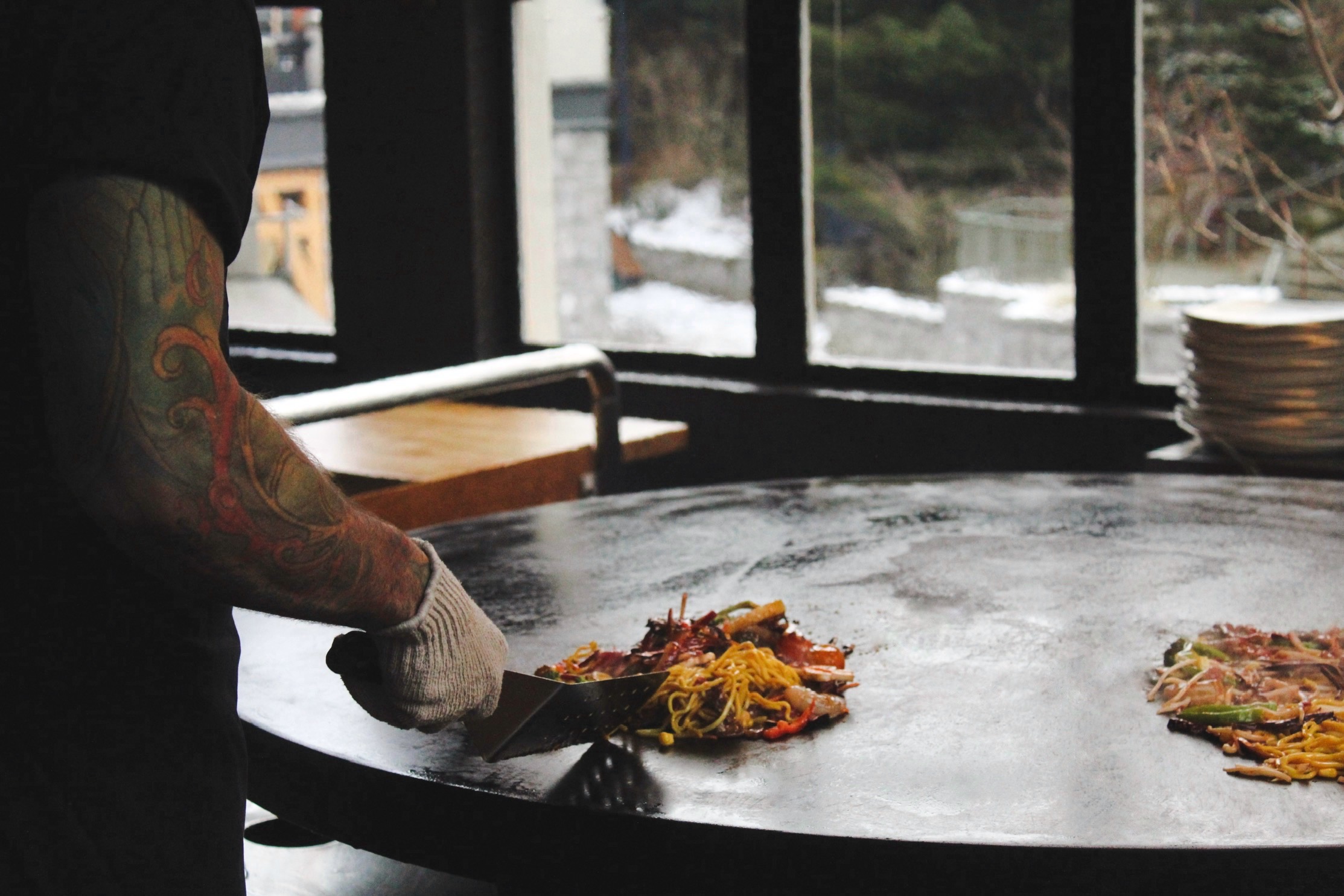 Tattooed chef grilling with snowy Whistler backdrop