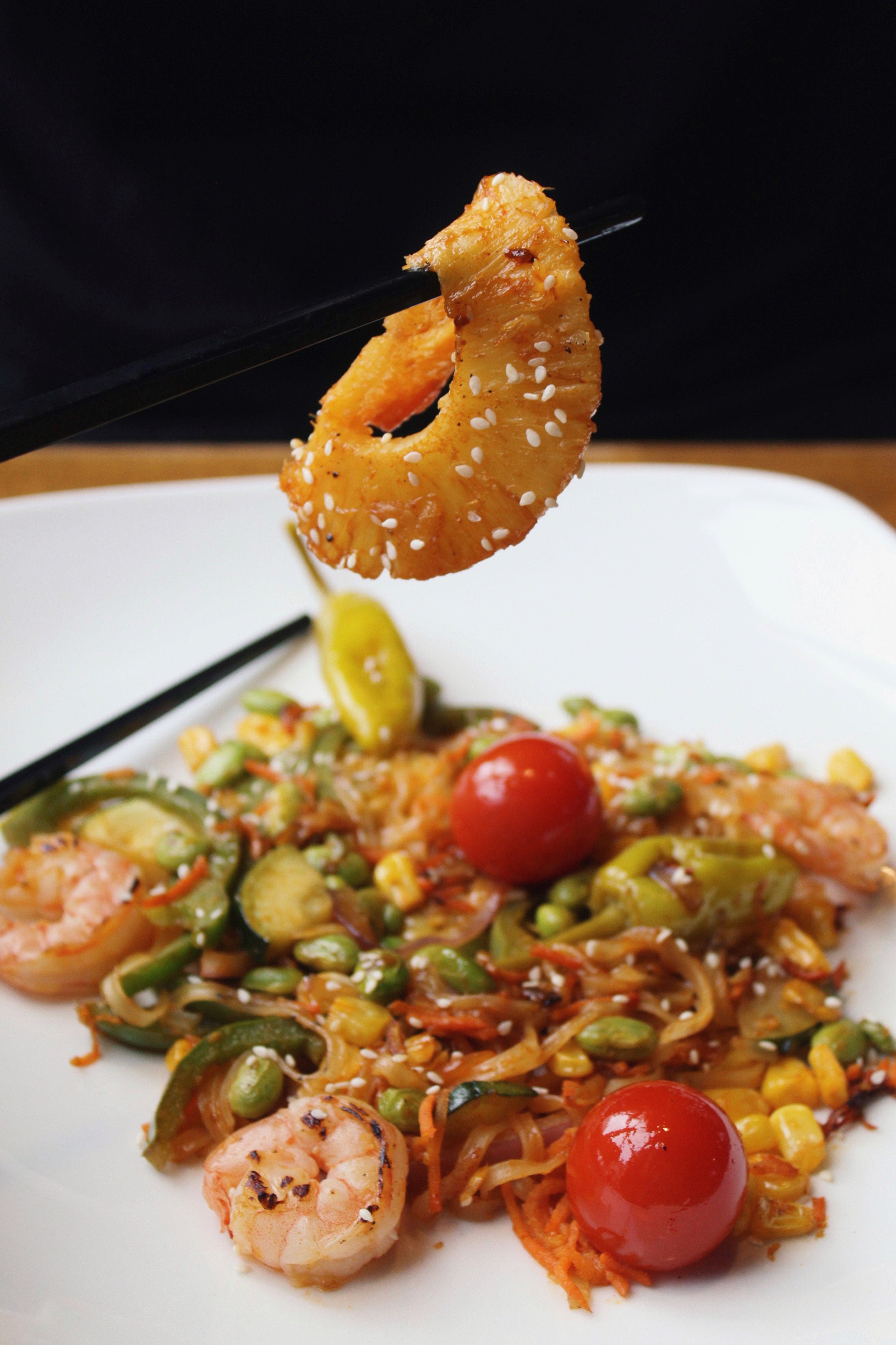 Shrimp on chopsticks over plated stir-fry